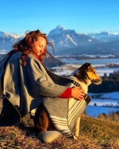 Denise Mayer sitzt auf einem Hügel mit Ihrem Hund. Beide sind in eine Decke gehüllt während Sie Ihren Hund freudig ansieht